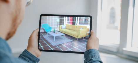 Decorating Apartment: Man Holding Digital Tablet with AR Interior Design Software Chooses 3D Furniture for Home. Man is Choosing Sofa, Table for Living Room. Over Shoulder Screen Shot with 3D Render
